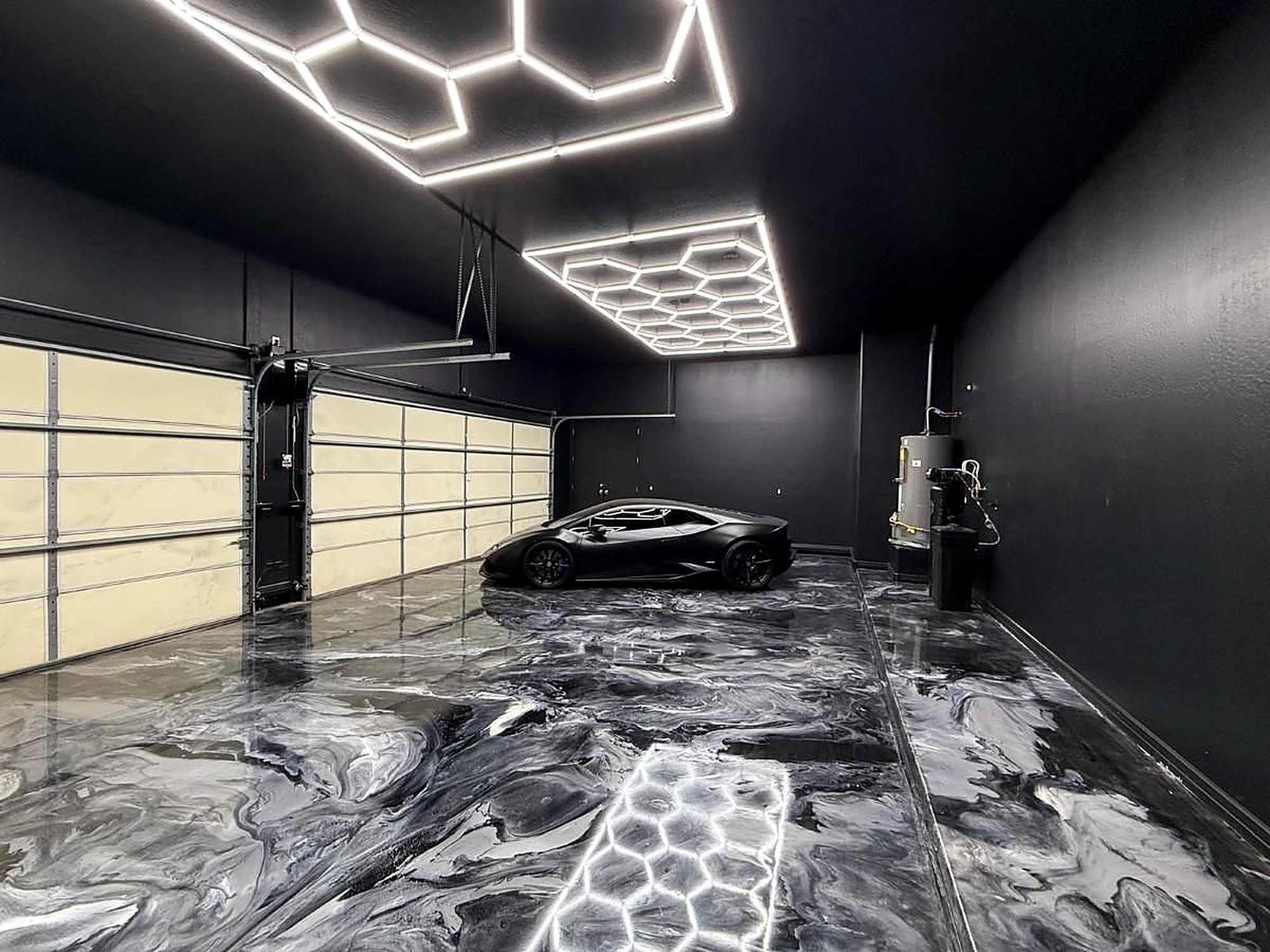 Black metallic epoxy garage floor with hex lighting and luxury car